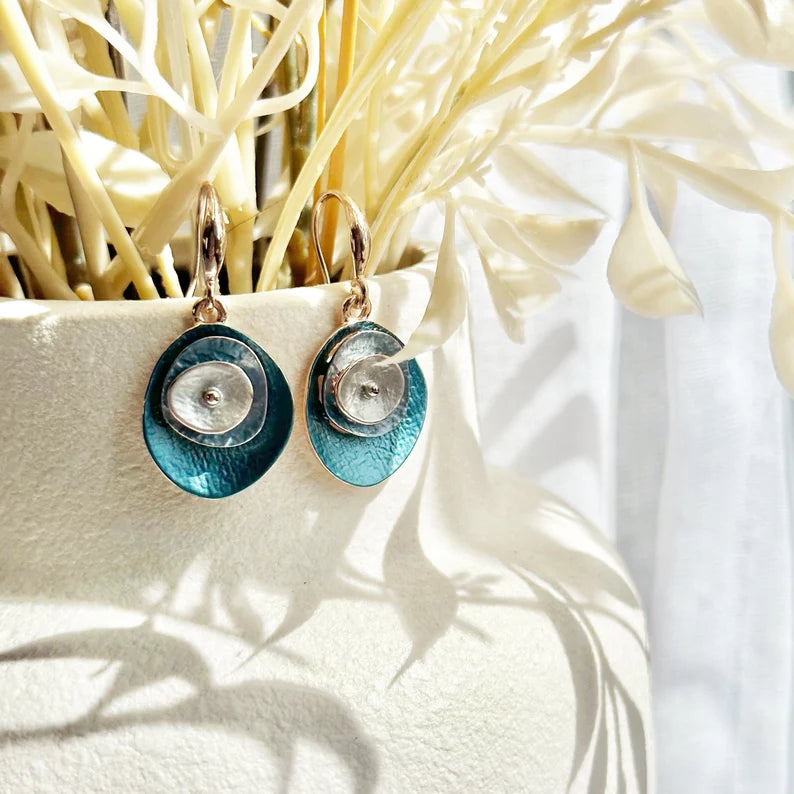 A pair of blue boho abstract flower earrings hand on the edge of a white vase with cream colored flowers. These earrings can be created in any color combination you like, making these the perfect gift to complete anyone's jewelry collection. These easy-breezy bohemian style layered disc dangle earrings are comfortable to wear and add a subtle pop of color. Wear them on their own, or go big and pair them with their matching abstract flower necklace.