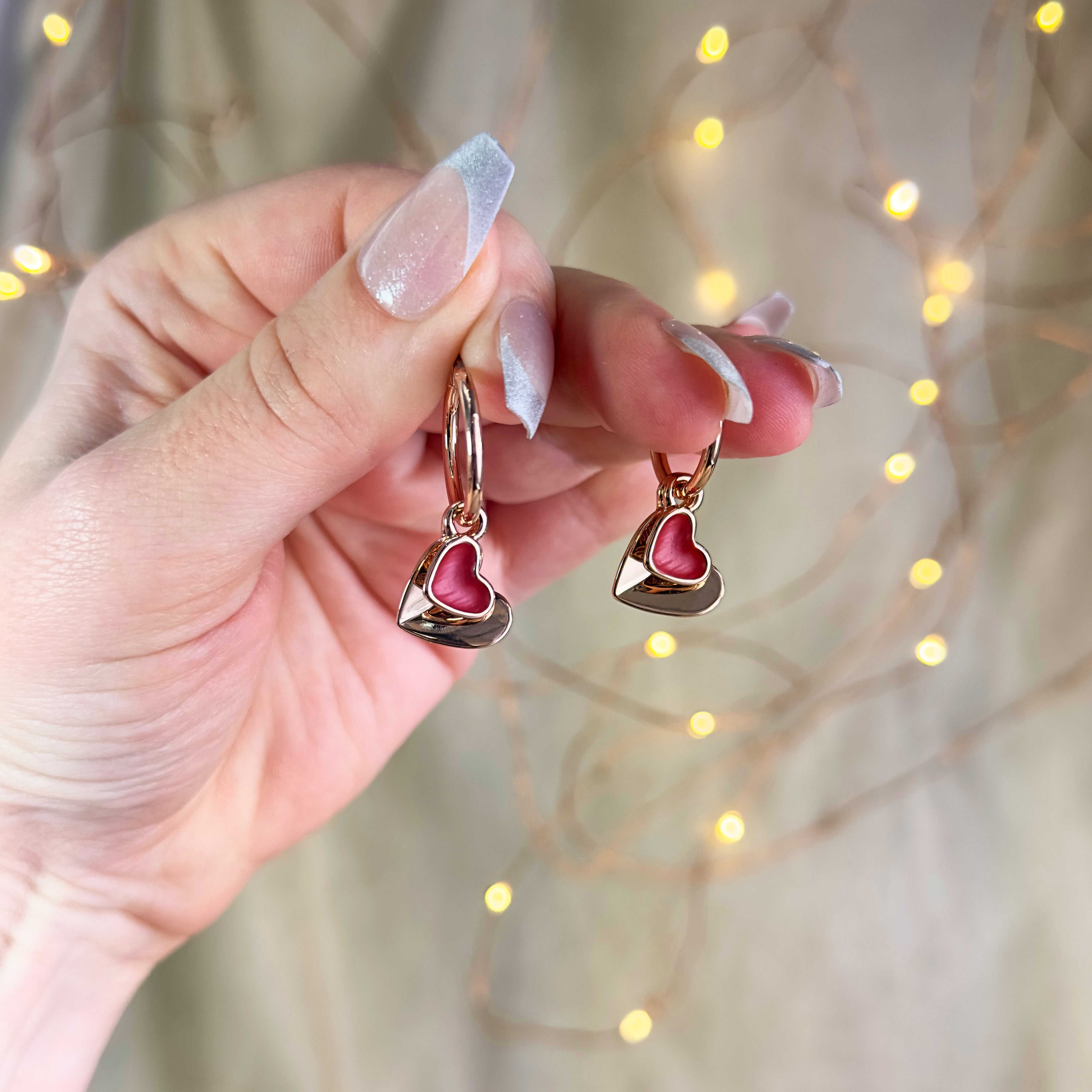 model holding Rose gold double hearts pendant hoop dangle earrings set on beige background. Heart charms, heart necklace, statement necklace, bohemian jewelry, boho jewelry