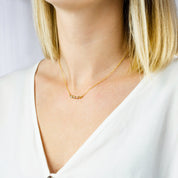 Model in white top is wearing a four stone dainty birthstone necklace featuring garnet, ruby, pink chalcedony and aqua chalcedony.