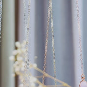 The camera pans down to reveal 3 bar necklaces with connected round birthstones, in silver, gold and rose gold. A person in a white shirt with long brown hair wears a gold bar necklace with "leighton" and a set of footprints engraved on the front with an attached yellow topaz citrine quartz birthstone. An up close shot of the bar pendant is shown. Finally, a silver bar necklace with an attached green amethyst birthstone is revealed in an open danique jewelry box.