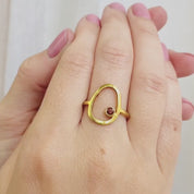 A person wears a single stone 3mm garnet open oval ring. This delicate egg shaped piece can be set with your choice of birthstone, with gemstone options for every month, plus alternative options if you want something a little different. Rings are available in gold, rose gold, or sterling silver and are hand crafted to your unique style. Birthstones available for January, February, March, April, May, June, July, August, September, October, November, December.
