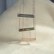 3 bar necklaces with the words mama, bestie and sister in cursive font with tails touching each end of the bar hand against a white background. Necklace metals available are sterling silver, rose gold, and gold filled. Each minimalist necklace can be custom engraved and is perfect for stand alone wear or layered with other necklaces. This simple bar necklace is the perfect I love you gift, birthday gift, Christmas gift, Mother's Day gift, anniversary gift, or just because gift.