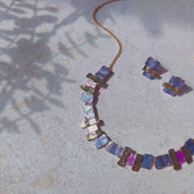This video features an array of creations from our Geometric Bohemian Collection. The first panover shows a geometric squares set of earrings and a necklace in pink and purple with a rose gold finish. A hand shows a set of geometric layered square earrings and a matching necklace. A person wears a geometric squares bangle bracelet in silver with teal and blue. A panover shows a sunray linear necklace in rose gold with yellow, blue and silver accent colors on the sun's "rays". Custom colors are available.