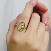 A person wears a 3-stone 3mm moonstone, clear quartz and kyanite open oval ring. This delicate egg shaped piece can be set with your choice of birthstone, with gemstone options for every month, plus alternative options if you want something a little different. Rings are available in gold, rose gold, or sterling silver and are hand crafted to your unique style. Birthstones available for January, February, March, April, May, June, July, August, September, October, November, December.