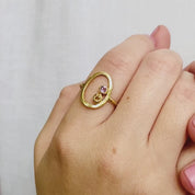 A person wears a 2-stone 3mm amethyst and citrine open oval ring. This delicate egg shaped piece can be set with your choice of birthstone, with gemstone options for every month, plus alternative options if you want something a little different. Rings are available in gold, rose gold, or sterling silver and are hand crafted to your unique style. Birthstones available for January, February, March, April, May, June, July, August, September, October, November, December.