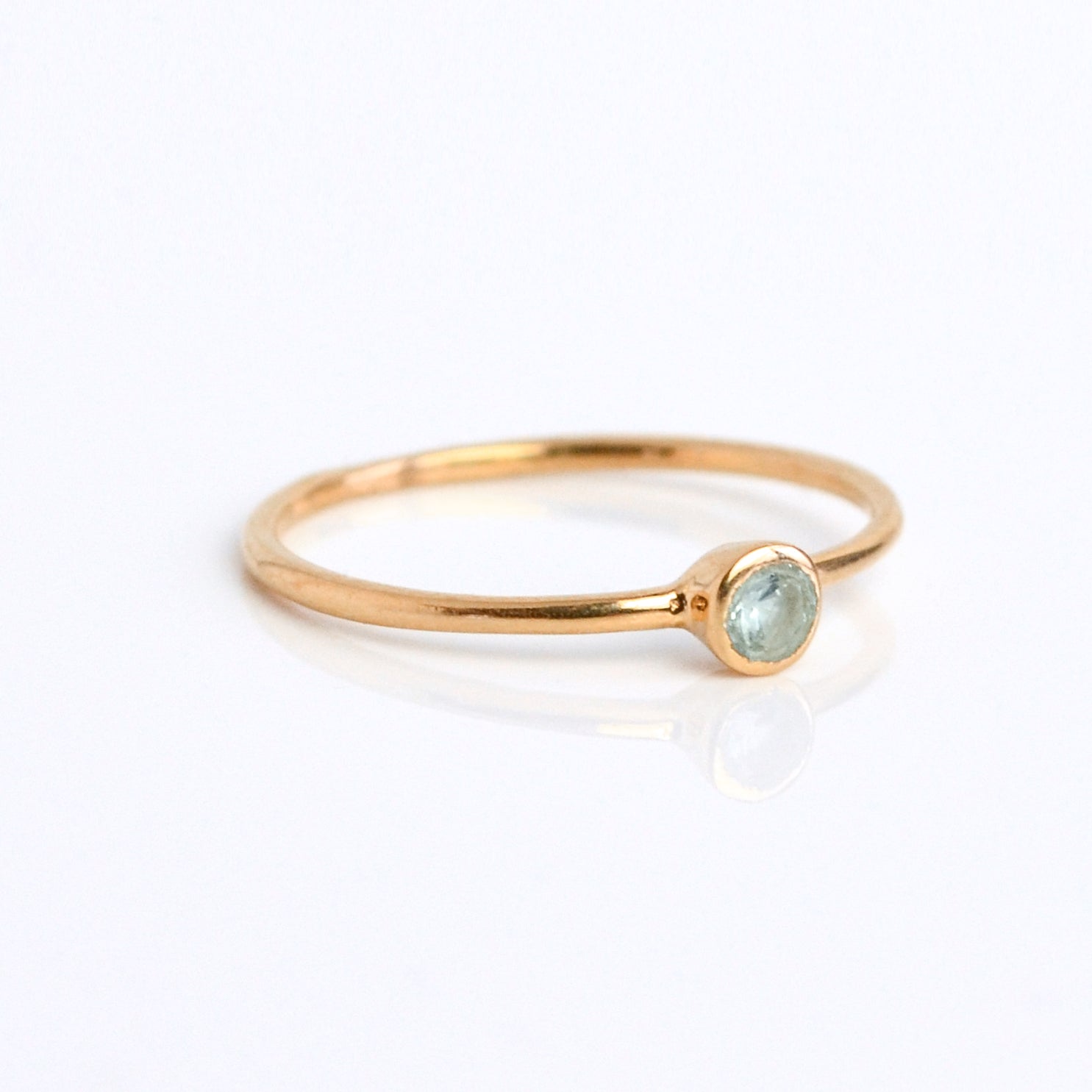 Single rose gold plated dainty 3mm blue topaz gemstone ring. December birthstone, on white background.