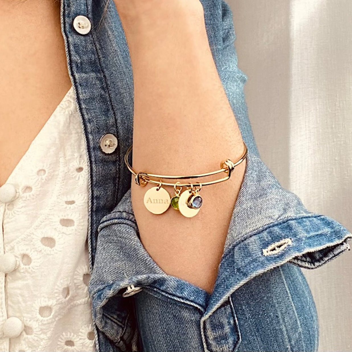 Model in white top and jean jacket is wearing out mother's bangle bracelet with engraved disk and peridot and kyanite birthstones.