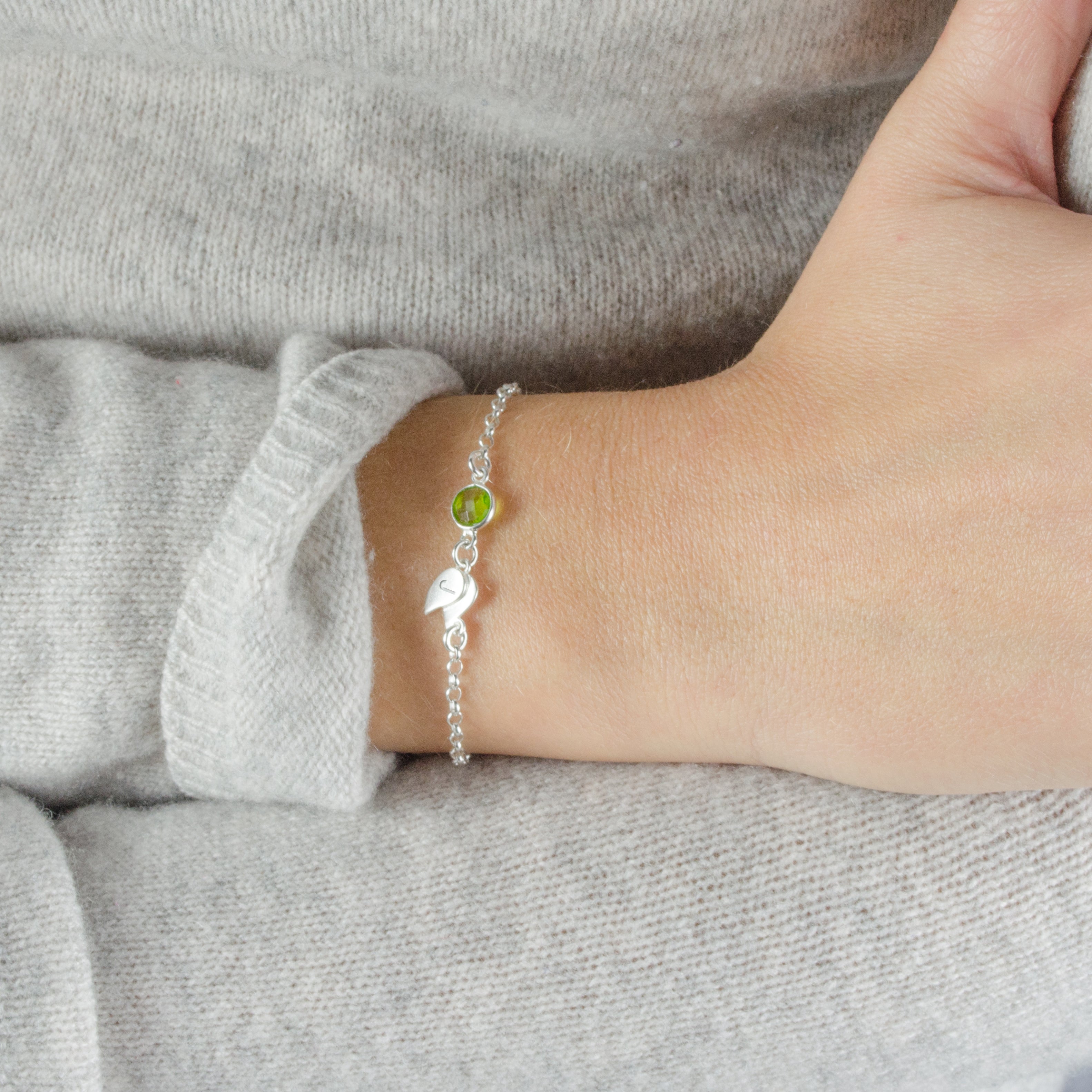 Model in white sweater is wearing a Single sterling silver double leaf initial charm with peridot birthstone. August birthstone, august gemstone, august birthday
