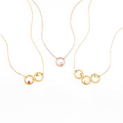 Collection of open circle eden necklaces from left to right. One gold filled necklace with ruby and peridot birthstones, one rose gold necklace with moonstone, and one gold necklace with pink chalcedony, moonstone and aqua chalcedony birthstones.