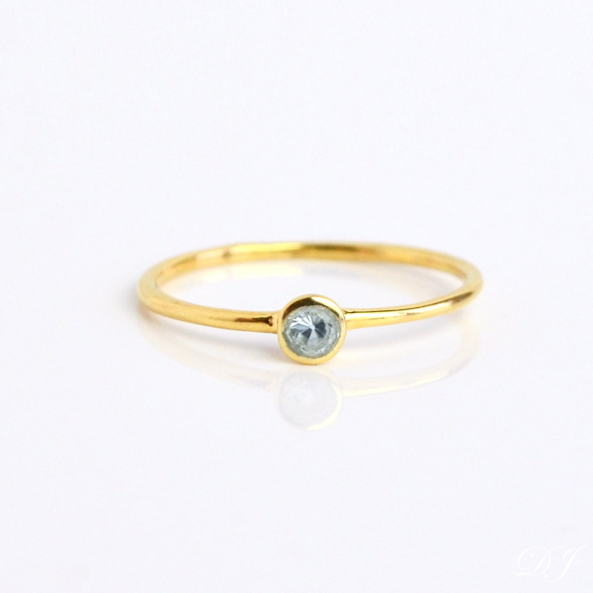 Single gold plated blue topaz gemstone dainty 3mm ring. December birthstone ring on white background.