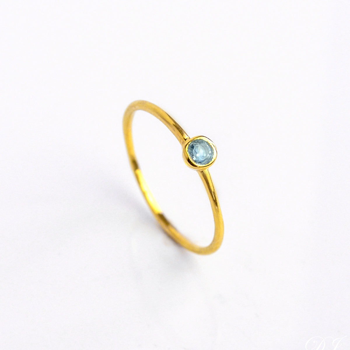 Single gold plated blue topaz dainty 3mm gemstone ring. December birthstone ring on white background.