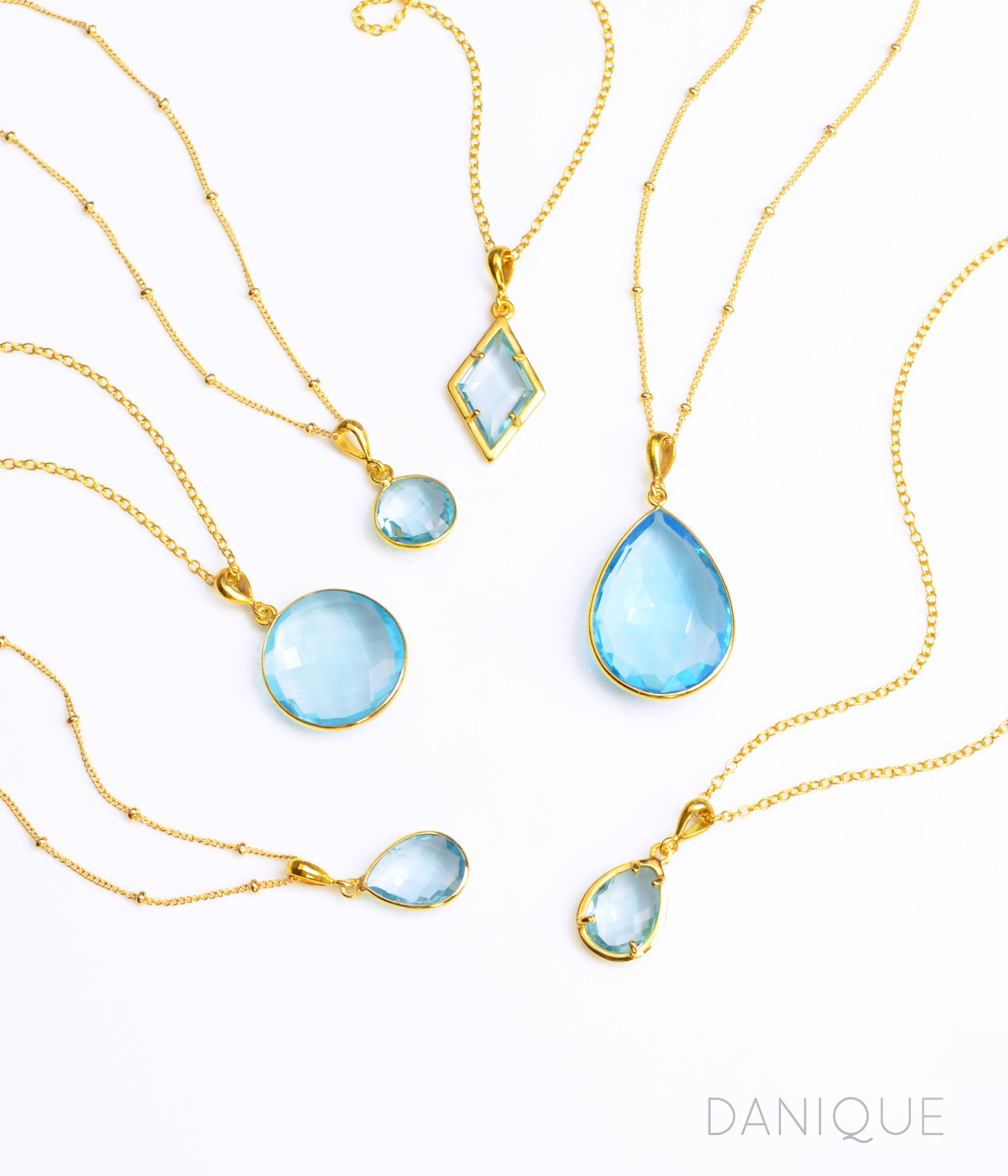 Shop our blue topaz necklace collection available in large, medium and small teardrops, prong set teardrop, prong set diamond, large and medium rounds on white background. Choose from satellite or cable chain. December birthstone.