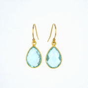 Gold blue topaz teardrop dangle earrings on a white background. Blue topaz birthstone, december birthstone, blue topaz gemstone, december gemstone.