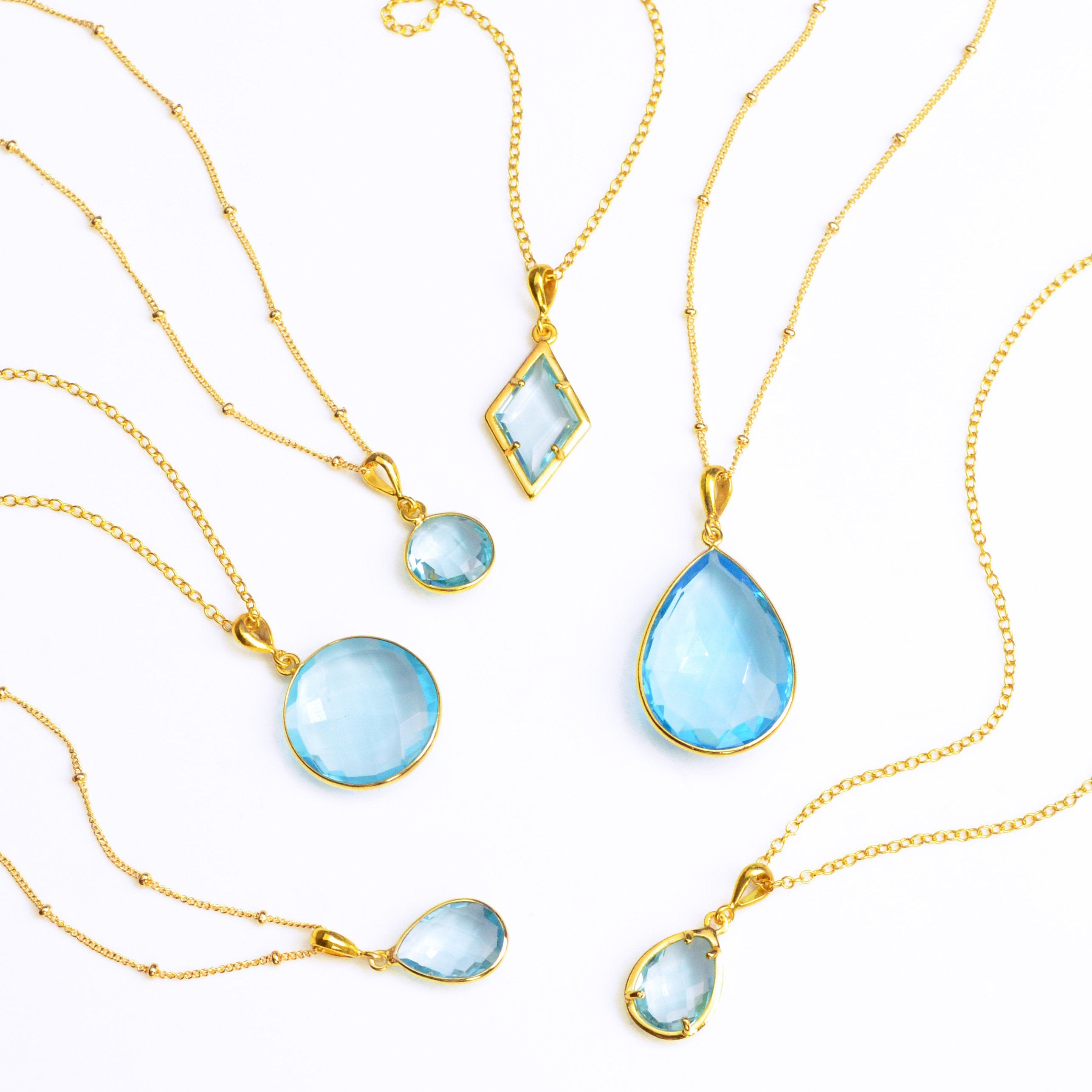 Shop our blue topaz necklace collection available in large, medium and small teardrops, prong set teardrop, prong set diamond, large and medium rounds on white background. Choose from satellite or cable chain. December birthstone.