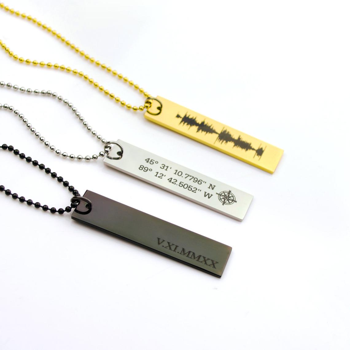 Collection of rectangle memorial tag necklaces in black with roman numerals, silver with a compass and coordinates or gold with a heartbeat engraved.