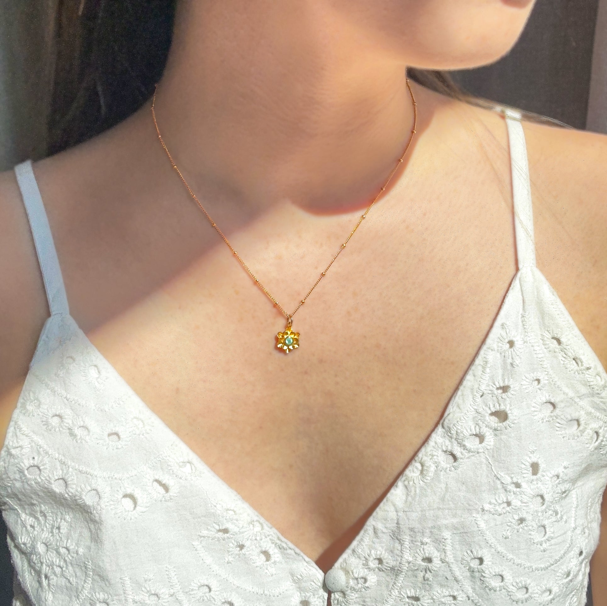 Model in white top is wearing a gold filled satellite chain flower bloom necklace with peridot birthstone.