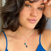 Lifestyle photo of a woman wearing the custon birthstone lariat necklace with blue and yellow birthstone drops resting at the collarbone. The piece showcases a slender chain, graceful movement, and subtle sparkle, perfect for office to evening.