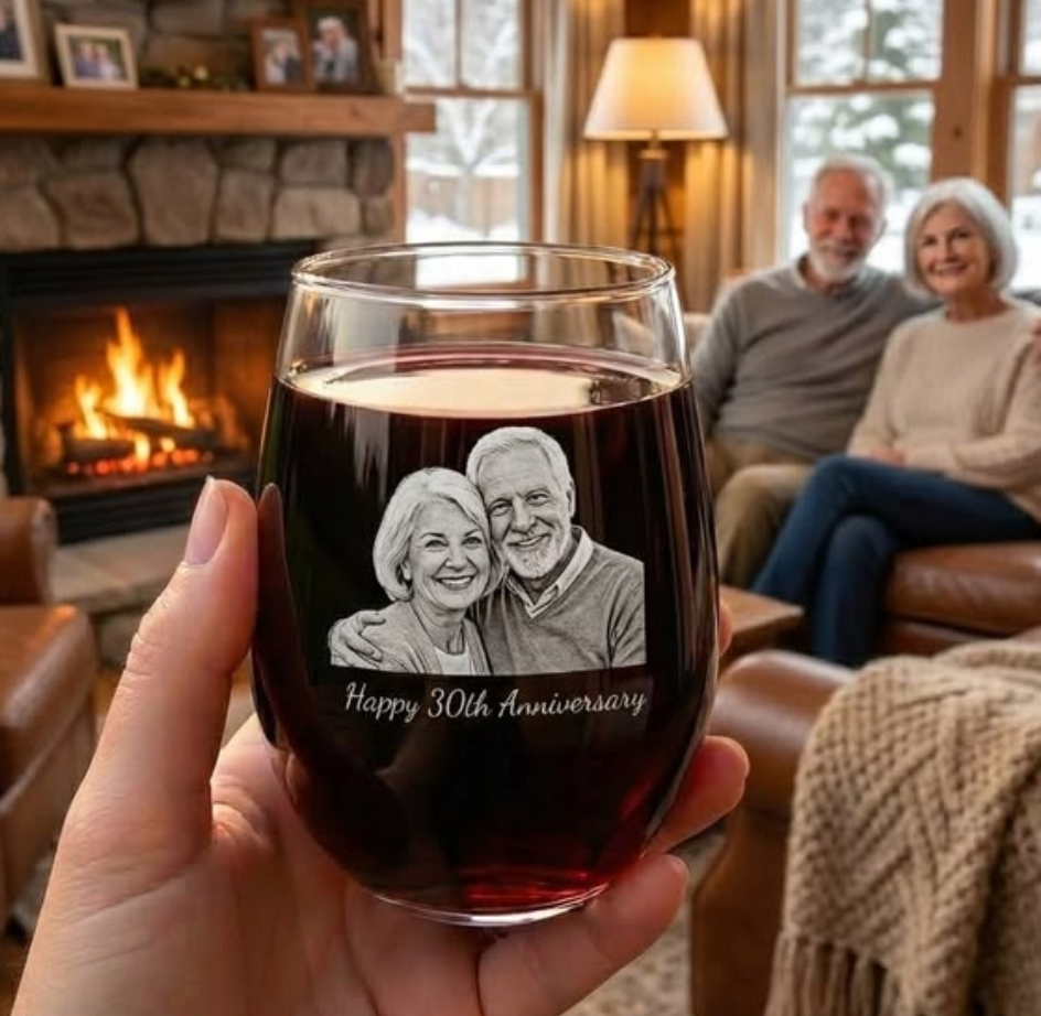 Personalized wine glass engraved with a couple’s photo and anniversary message, filled with red wine and held in front of a cozy fireplace scene, a meaningful custom anniversary gift for couples and wine lovers.
