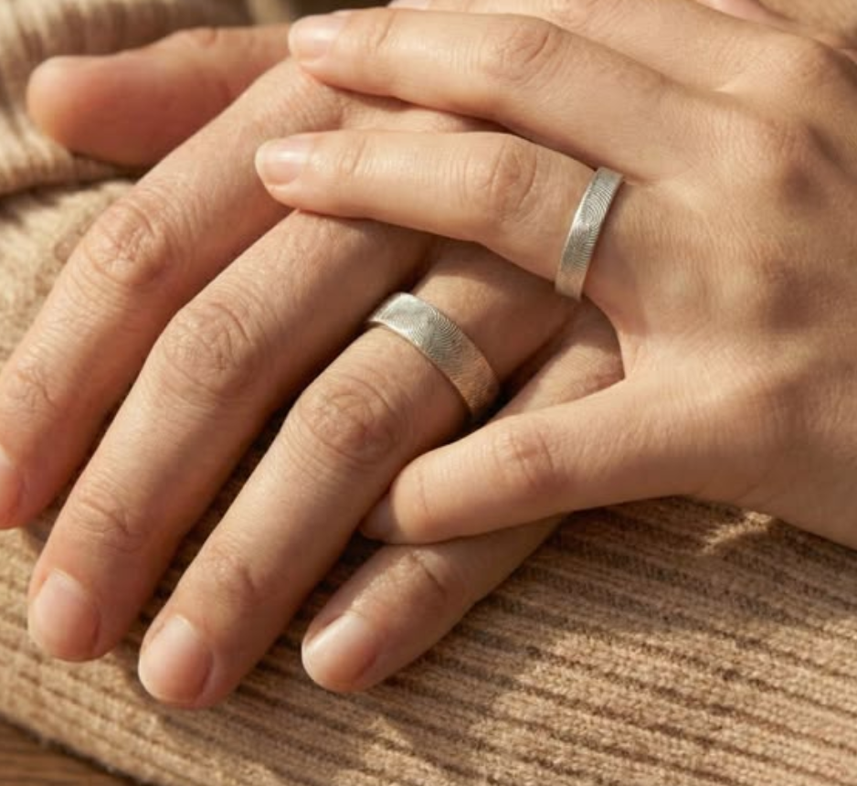 Close-up of couple holding hands wearing matching engraved fingerprint rings, minimalist silver bands symbolizing love, commitment, and connection, personalized couples jewelry for weddings or anniversaries.