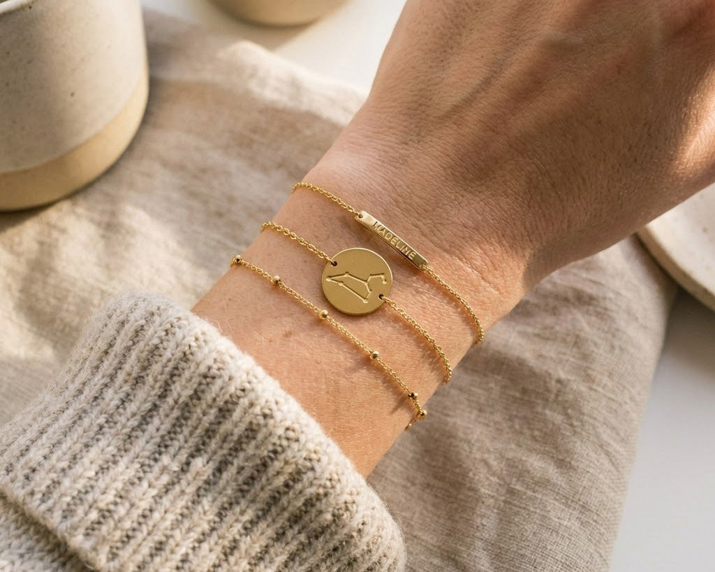 Minimalist gold zodiac constellation bracelet engraved with star pattern layered with delicate chain bracelets on a model’s wrist, elegant celestial astrology jewelry styling gift for zodiac lovers