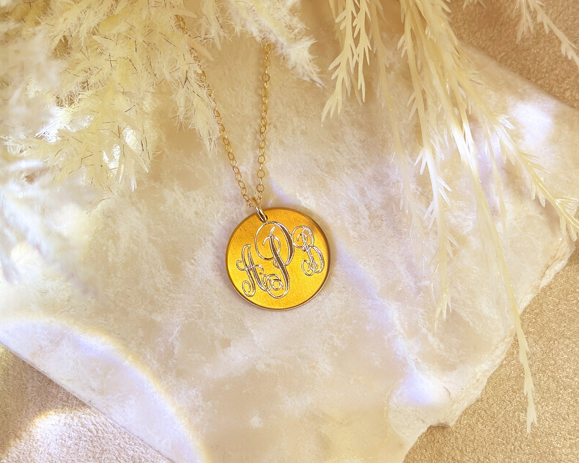 Gold monogram disk necklace with engraved script initials on a delicate chain, displayed on soft neutral fabric and pampas grass – personalized jewelry gift for her, girlfriend, student, or new job celebration, milestone gift