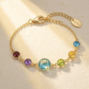 Custom birthstone mom bracelet with colorful gemstone charms representing children, featuring a larger center stone for mom on a delicate gold chain.