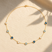 Long birthstone station necklace with blue and white natural gemstones arranged on warm beige fabric