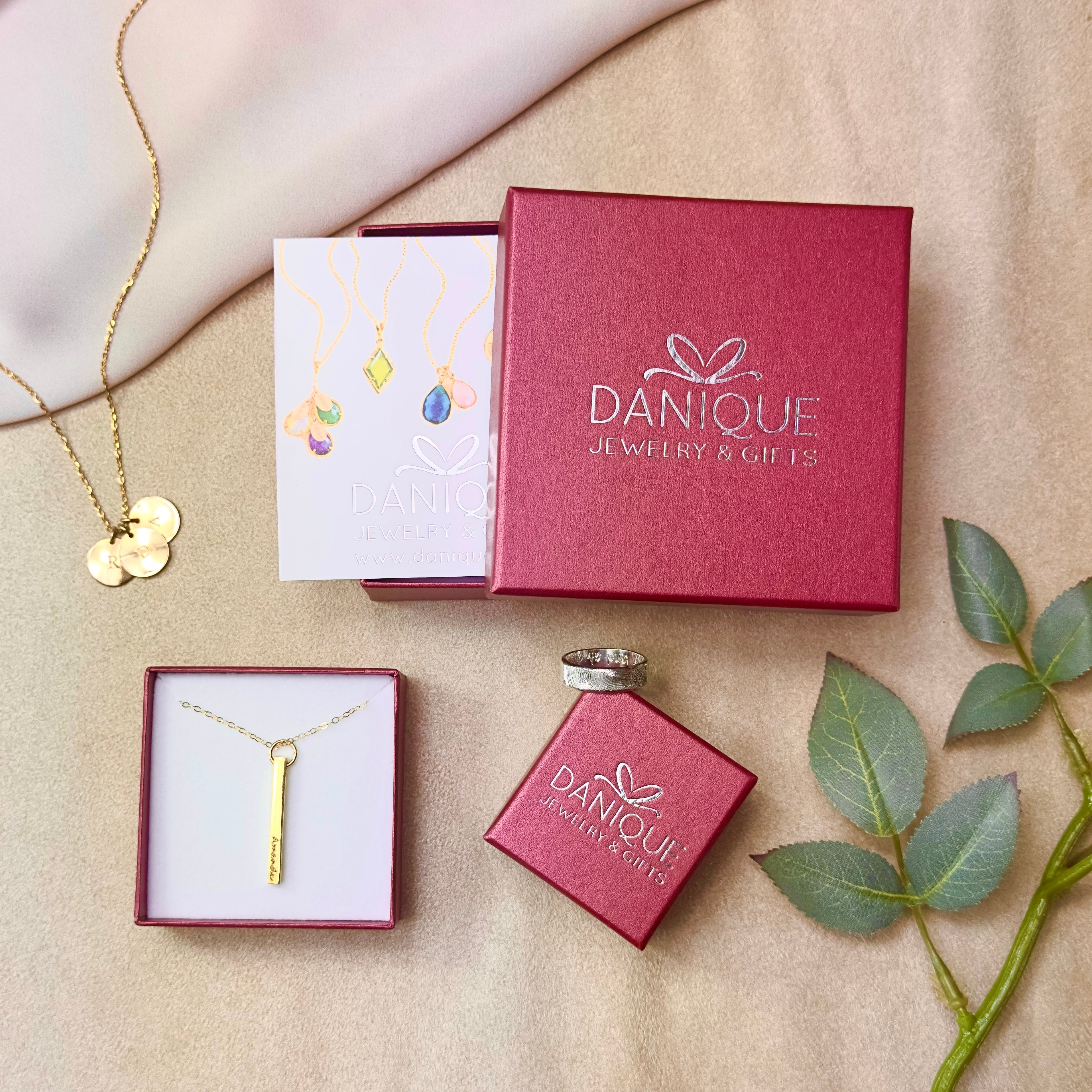 3 red danique jewelry boxes show custom engraved personalized gold and silver jewelry. A red box with a danique jewelry post card peeks out of the center square box. Custom engraved gifts, personalized gifts for women, mom gift, memorial gift, monogrammed gifts.