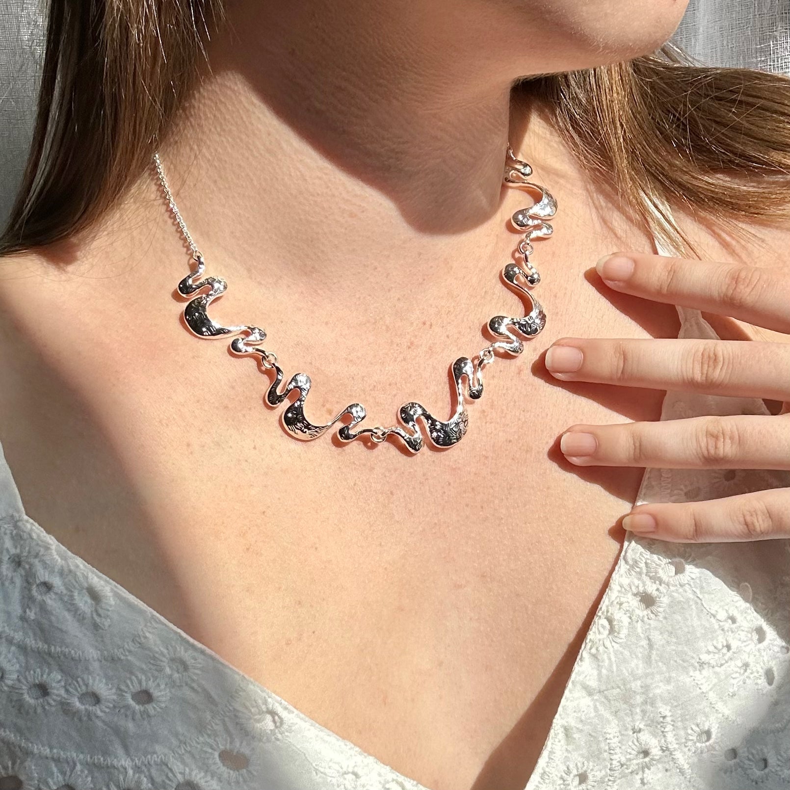 Adjustable Silver Necklace with a cable chain and five textured wave pendants connected by silver jump rings is worn by a model in a white blouse