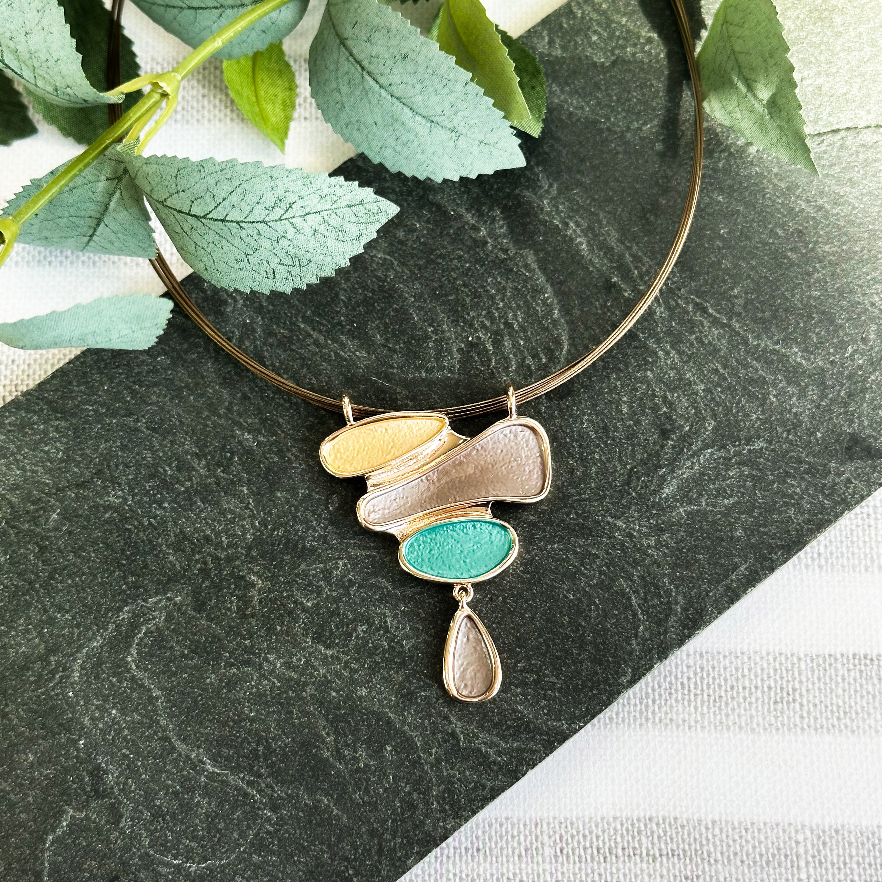 Rose Gold Boho Style Pendant Necklace with dangling Teardrop painted in gold, brown and teal Rests on a black stone with leaves in the background. Abstract Necklace for Her, Gift for Mom, Mother&#39;s Day Gift.