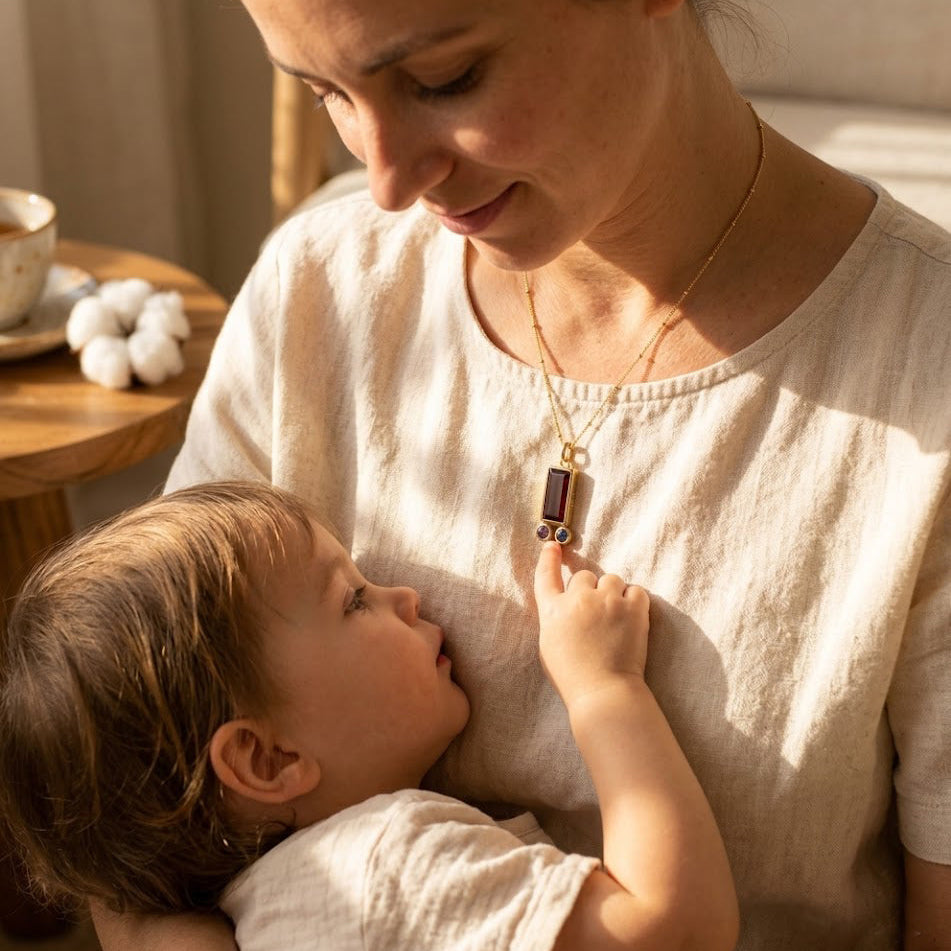 Close-up of custom birthstone mom necklace with opal-style baguette charm and tiny purple and golden birthstone charms for children on a dainty chain.