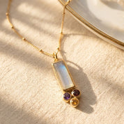 Custom mom birthstone necklace with a baguette birthstone pendant representing mom and tiny round birthstone charms representing kids, shown on a delicate gold chain.