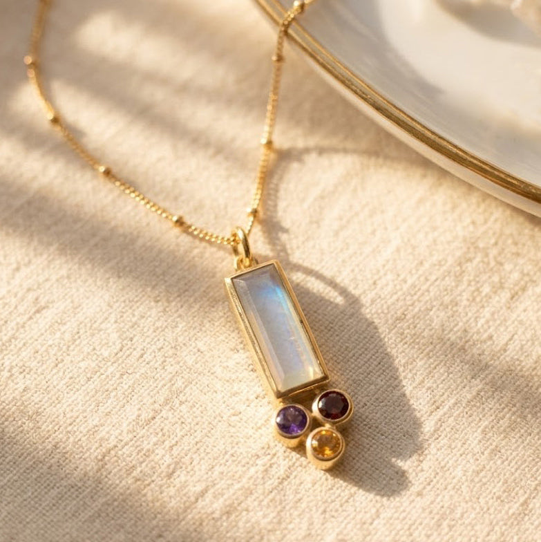 Custom mom birthstone necklace with a baguette birthstone pendant representing mom and tiny round birthstone charms representing kids, shown on a delicate gold chain.