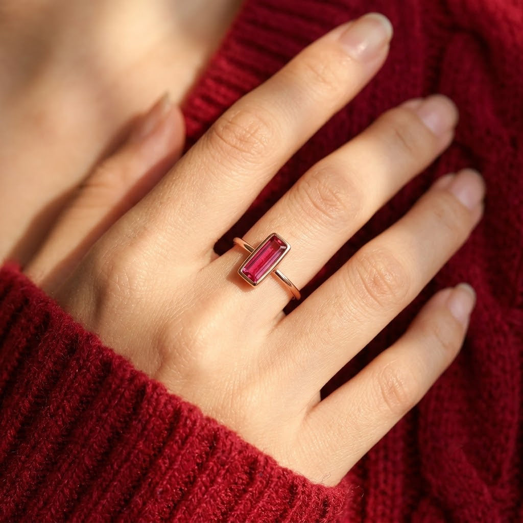 Tiny ruby quartz baguette ring worn on a model’s hand with a burgundy sweater.