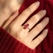 Tiny ruby quartz baguette ring worn on a model’s hand with a burgundy sweater.
