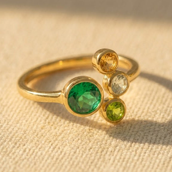 Adjustable family birthstone ring with one larger Mom gemstone and three petite children’s stones displayed in warm natural light.