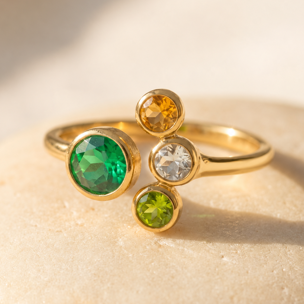 Adjustable birthstone ring for Mom of three with one large green gemstone and three smaller children’s birthstones in yellow gold.
