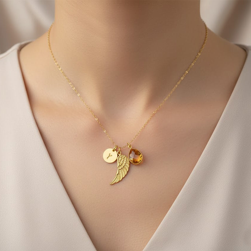Woman wearing angel wing birthstone necklace with engraved initial charm, handcrafted in vermeil gold and sterling silver, designed as a personalized remembrance jewelry gift.