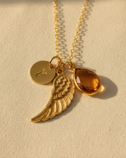 Personalized angel wing necklace featuring a natural birthstone teardrop, engraved initial disk, and gold vermeil wing charm, a meaningful memorial jewelry piece and sympathy gift for women.