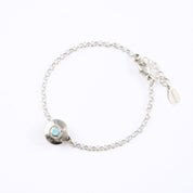 A 925 sterling silver donut bracelet with an aqua chalcedony stone and the letter "M" engraved on the bottom of the disc rests against a white background. This bracelet is hypoallergenic and is sure to make the day of anyone who receives this as a gift! This is the perfect thing for Mother's Day! 