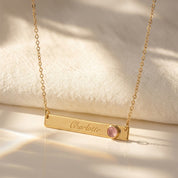 Personalized gold birthstone bar necklace engraved with name and pink gemstone
