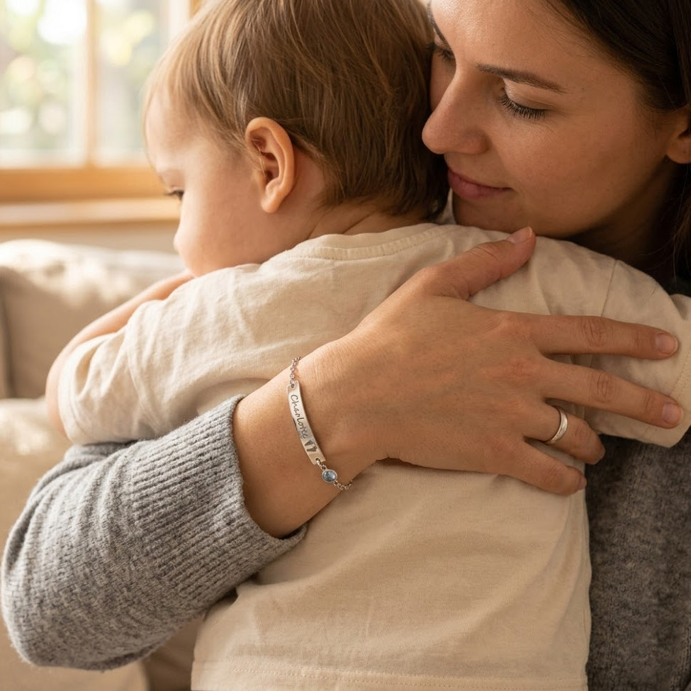 Engraved baby footprint bracelet with aquamarine March birthstone, set on satin fabric. Customizable with footprints, names, or initials. Unique gift for moms, grandmas, and daughters. Dainty handmade jewelry keepsake.