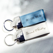 Two keychains at a diagonal angle rest on a textured cloth background. A silver blue keychain says I Love You in Sunshine font with stars on each side. A white keychain says Sarah (heart) Bobby in Grace font.Leather Keychain White Blue Magenta Brown Zinc Alloy Metal Keyrings Personalized Gift Personalized Key Fob College Dorm Gift College Grad Gift Graduation Gift for Him or Her Natural Leather Custom Gift for Women