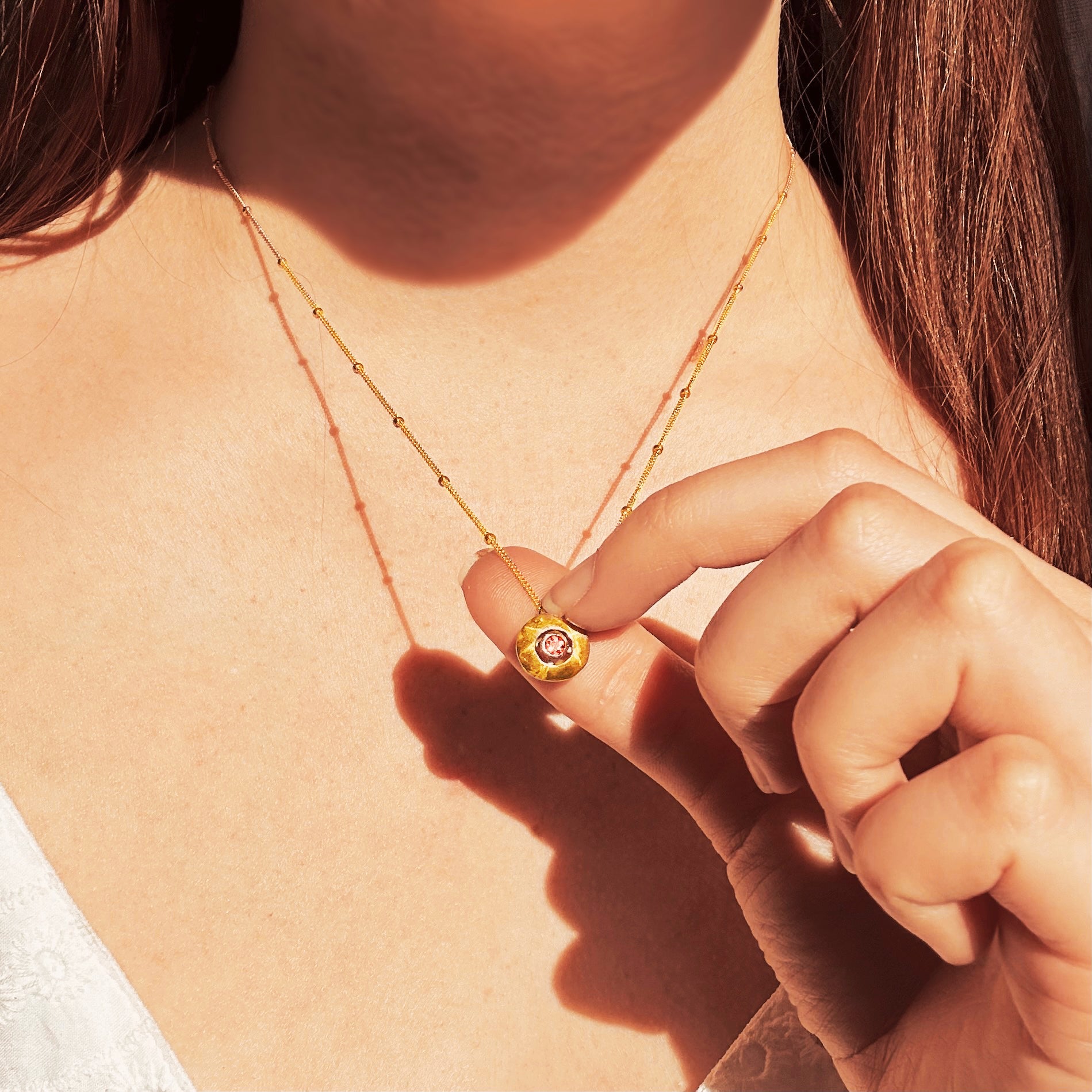 Model wears necklace with a 14k gold filled satellite chain and a circular pendant with July birthstone Ruby bezel set in the center. Pendant can be custom engraved with initials.