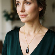 Woman wearing a large Black Onyx teardrop gemstone necklace with a dark green blouse.
