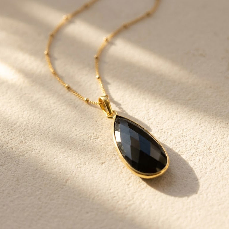 Natural Black Onyx large teardrop pendant necklace in yellow gold with faceted black gemstone on a delicate chain.
