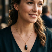 Woman wearing a Black Onyx teardrop pendant necklace in yellow gold with an elegant dark outfit.
