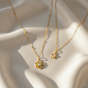 mother daughter birthstone flower necklace set with two gold bloom pendants resting on soft champagne satin, larger layered flower pendant with aqua blue center stone and smaller dainty blossom with pale pink birthstone, both on delicate gold chains catching warm sunlight, personalized birthstone flower necklaces available in sterling silver or gold filled, meaningful matching jewelry gift for mom and daughter, grandma and granddaughter, birthday, Mother’s Day or holiday