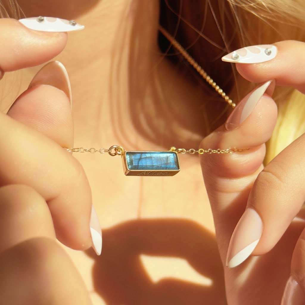 Close-up of faceted blue labradorite bar necklace in a gold bezel setting held in natural sunlight