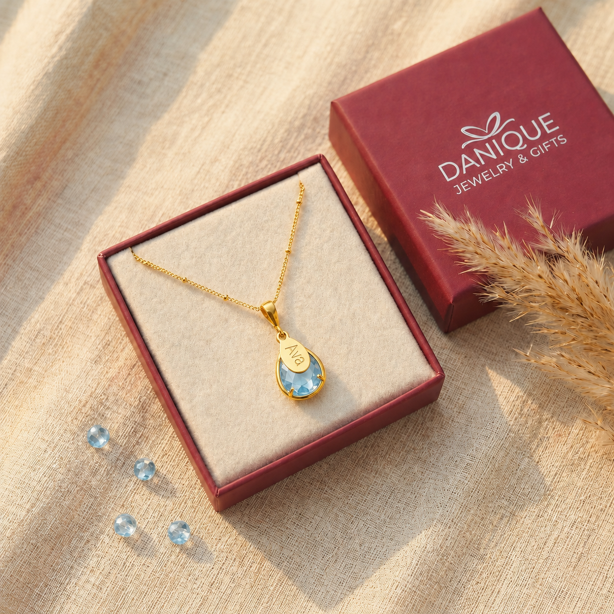 Personalized blue topaz name necklace displayed in a burgundy Danique Jewelry gift box